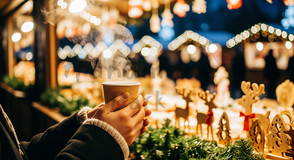 フリー素材 無料 写真｜屋外のクリスマスマーケットで温かい飲み物を手にする日本人の手元、無地カップと灯りのにぎわいが映える冬の屋台風景 背景素材