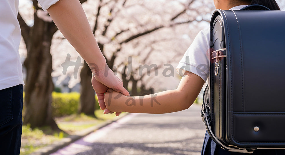 フリー素材 無料 写真｜桜の下で手をつなぐ親子の手元、無地ランドセルで匿名性 背景素材