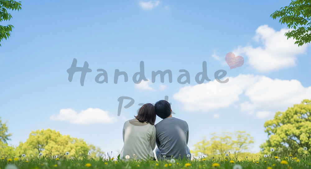 フリー素材 無料 写真｜芝生で肩を寄せる日本人カップルの後ろ姿青空と穏やかな時間のイメージ