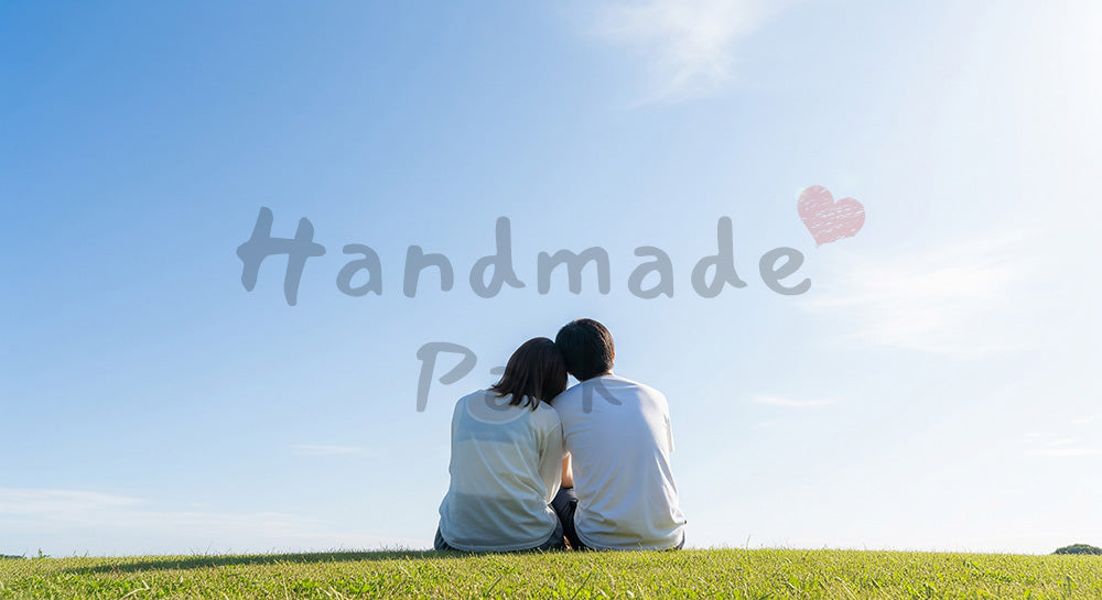 フリー素材 無料 写真｜青空と穏やかな時間のイメージのある芝生で肩を寄せる日本人カップルの後ろ姿