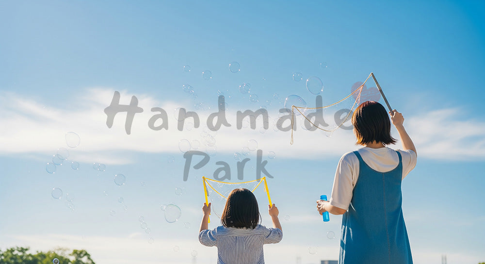 フリー素材 無料 写真｜青い空にシャボン玉を飛ばす日本人親子の後ろ姿、やさしい公園の休日