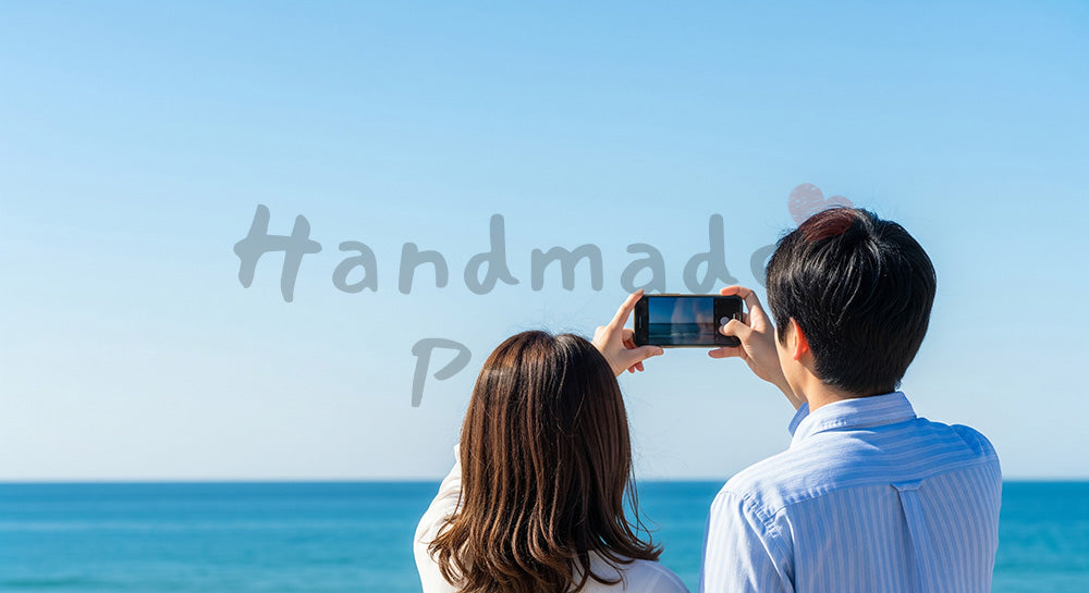 フリー素材 無料 写真｜海辺で景色を撮る日本人カップルの後ろ姿、青空と旅のワクワク感の空きスペース 背景素材
