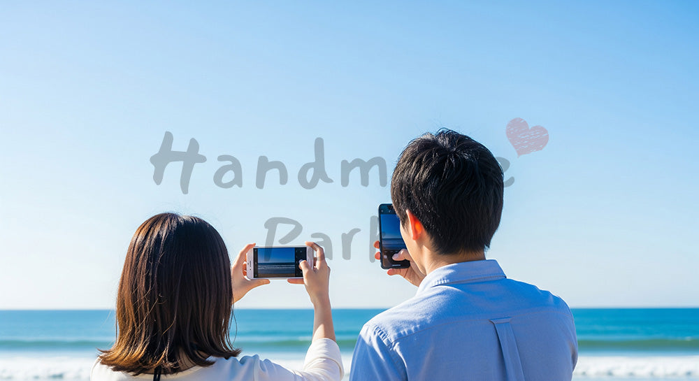 フリー素材 無料 写真｜海辺で景色を撮る日本人カップルの後ろ姿、青空と旅のワクワク感のスペース